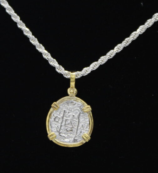 The Treasure Shoppe Inc. presents the Gold Plated Reale/Oblong Coin - Atocha Shipwreck Coins pendant, featuring an ancient coin in a gold-plated frame with four prongs and intricate, faded carvings set against a black background.
