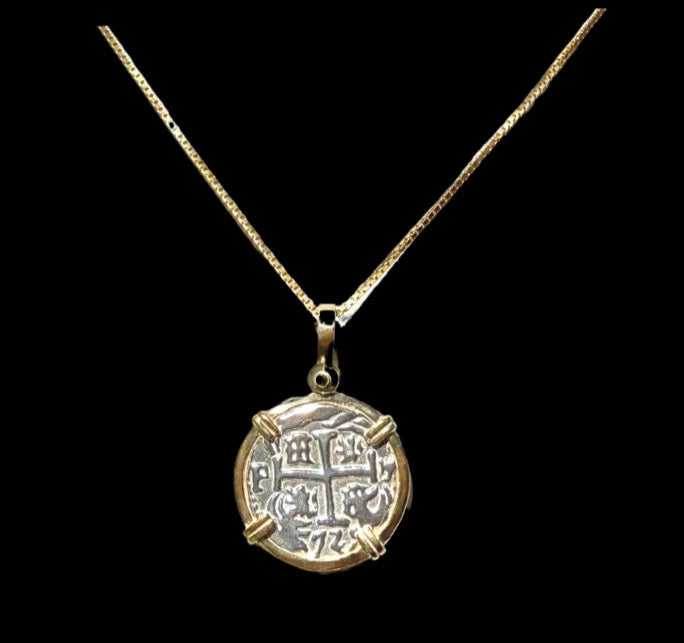 The Treasure Shoppe Inc.s Gold Plated Round Reale Coin-Atocha Shipwreck Pendant features engraved symbols and a cross pattern, secured by four prongs. Its reminiscent of an Atocha coin and displayed against a black background.