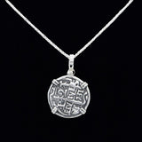 The Treasure Shoppe Inc.s Silver Round Reale Coin- Atocha Shipwreck Coins pendant features a round coin-like medallion with an abstract design, set in a sterling silver bezel and displayed against a black background, minus the chain.