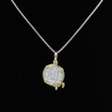A silver chain necklace features The Treasure Shoppe Inc.s Gold Plated Small Turtle Coin- Atocha Shipwreck Pendant, capturing historic charm with its ornate gold-tone frame against a black background.