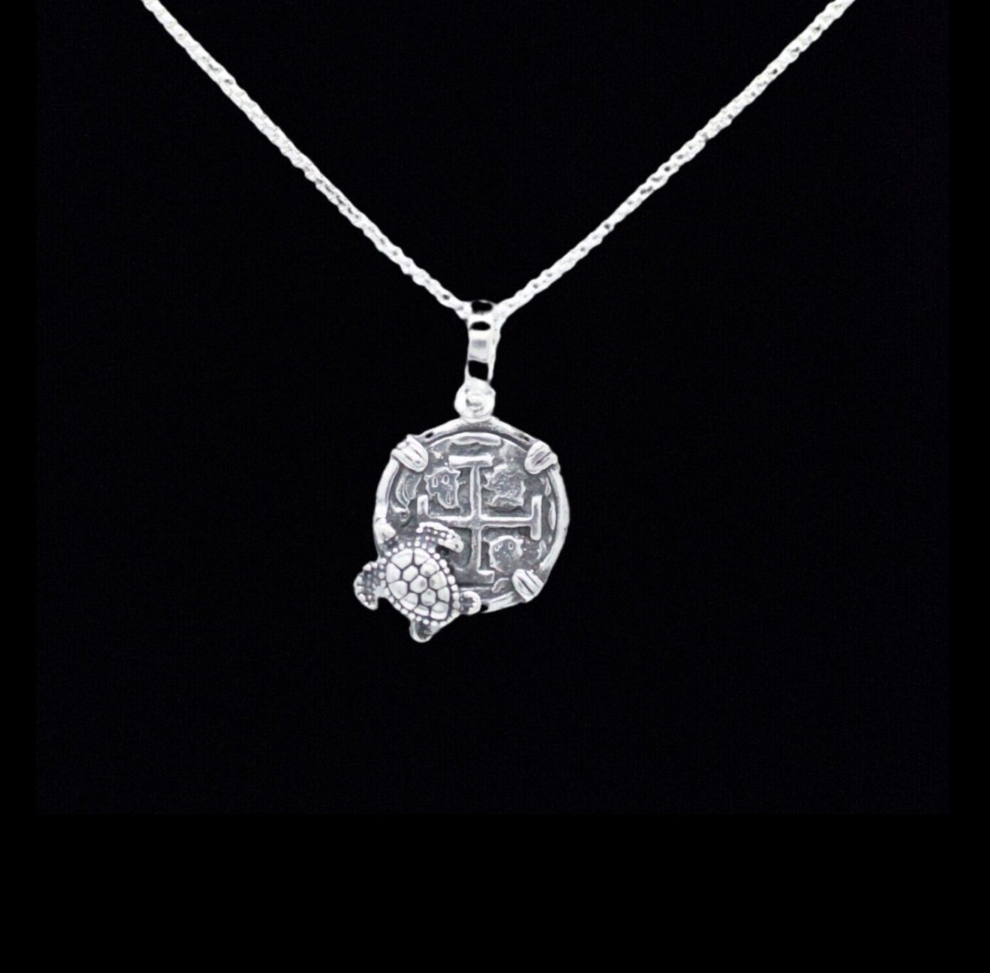 The Silver Small Turtle Coin by The Treasure Shoppe Inc. features a turtle on a textured coin surface inspired by Atocha shipwreck coins, framed in a sterling silver bezel against a striking black background.