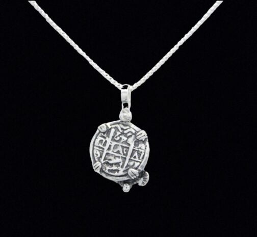 The Treasure Shoppe Inc.s Silver Small Turtle Coin from the Atocha Shipwreck is elegantly mounted in a sterling silver bezel, featuring engraved symbols and resting against a black background.