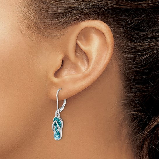 A close-up of a woman with light to medium skin and pulled-back hair wearing Presco/Quality Golds Crystal Flip Flop Dangle Earrings, sterling silver earrings adorned with blue crystals and shaped like flip-flop sandals.