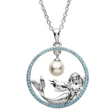 The Shanore Swarovski Crystals Circle Mermaid with Pearl Necklace features a mesmerizing mermaid pendant within a gem-studded circular frame. The enchanting mermaid holds a central pearl, completing this elegant piece of ocean jewelry.