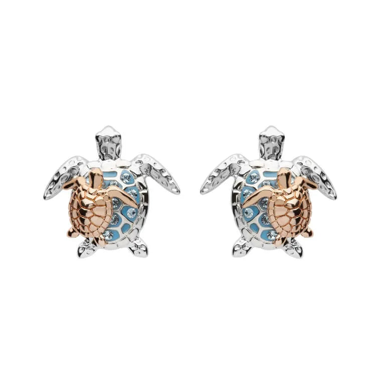 The Shanore Swarovski Crystals Turtle & Baby Stud Earrings feature two turtle-shaped studs in sterling silver with gold accents. Their blue-detailed shells and sparkling crystals stand out against a white backdrop, exuding elegance.