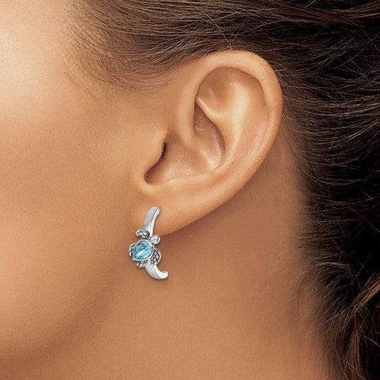 A close-up of a woman’s ear wearing Presco/Quality Gold Crystal Half-Hoop Post Turtle Earrings, featuring sterling silver with blue gemstone accents, against a neutral background.