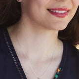 A person wears a smile and the Holly Yashi Green Flash Bella Butterfly Necklace, along with matching earrings. Both feature green butterfly pendants. The necklaces sterling silver chain adds elegance, complementing their subtly patterned dark top as part of their face is visible.