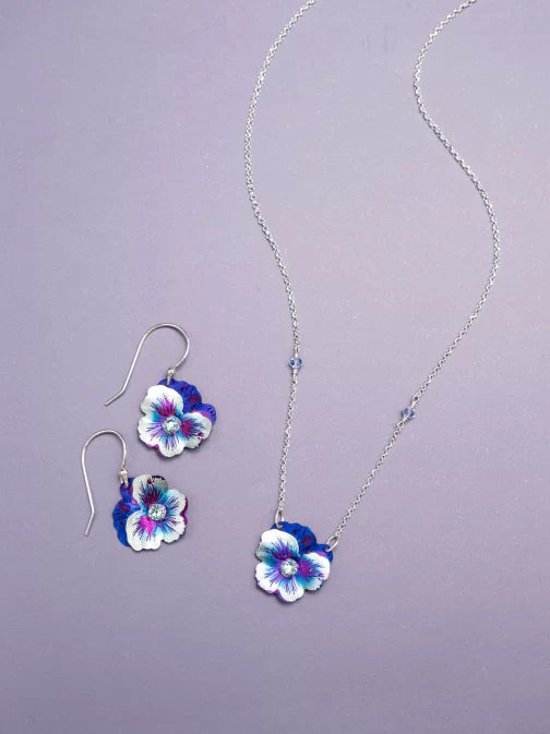 Discover the elegance of this jewelry set featuring a silver chain necklace and Holly Yashis Sparkling Fuchsia Garden Pansy Drop Earrings with stunning purple and white flower pendants on a light purple background.