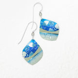 The Lani Kai Blue Earrings by Holly Yashi feature handcrafted square dangles with silver hooks, displaying blue, light blue, and gray floral and leaf patterns on a white textured background.