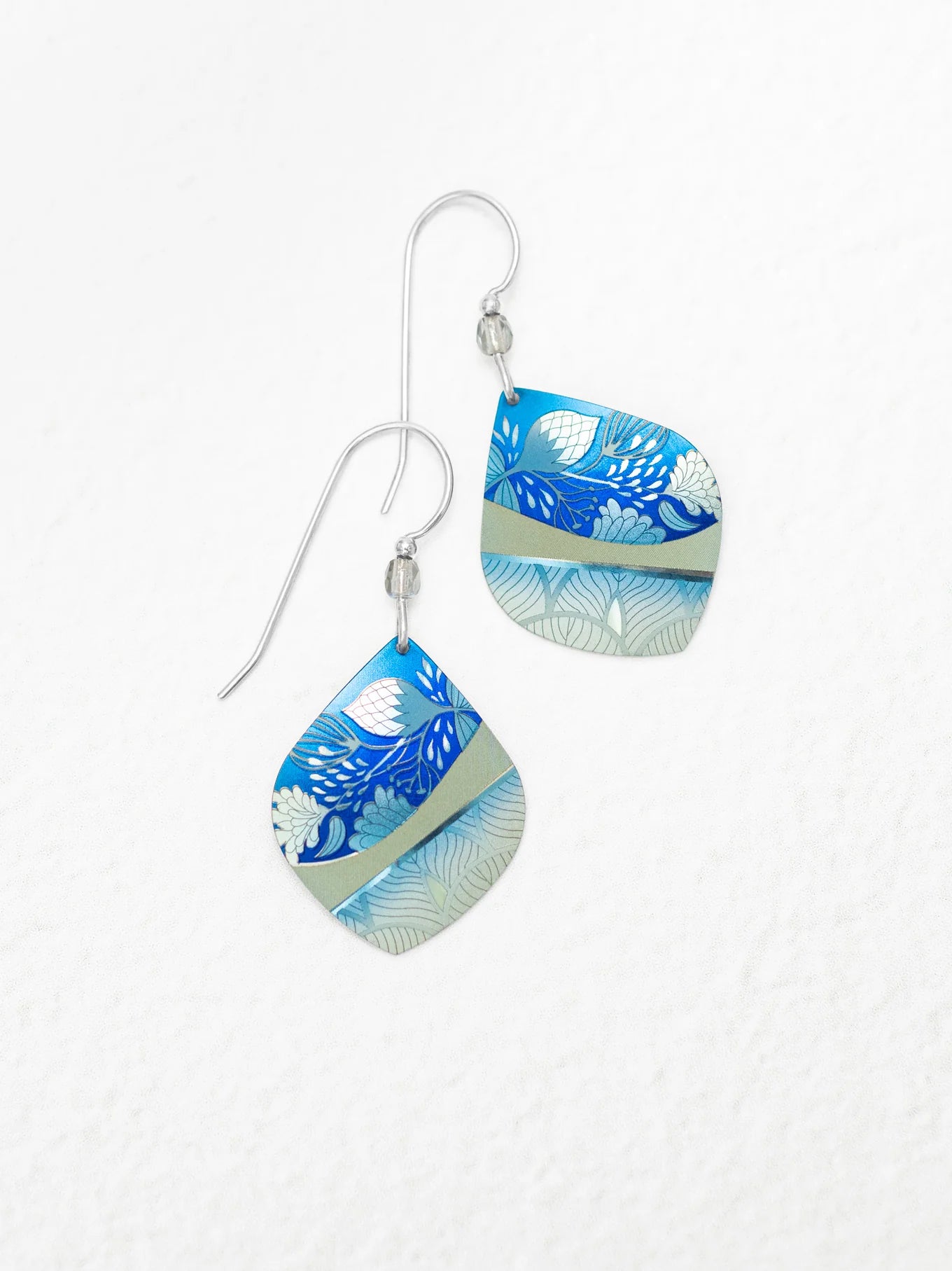The Lani Kai Blue Earrings by Holly Yashi feature handcrafted square dangles with silver hooks, displaying blue, light blue, and gray floral and leaf patterns on a white textured background.