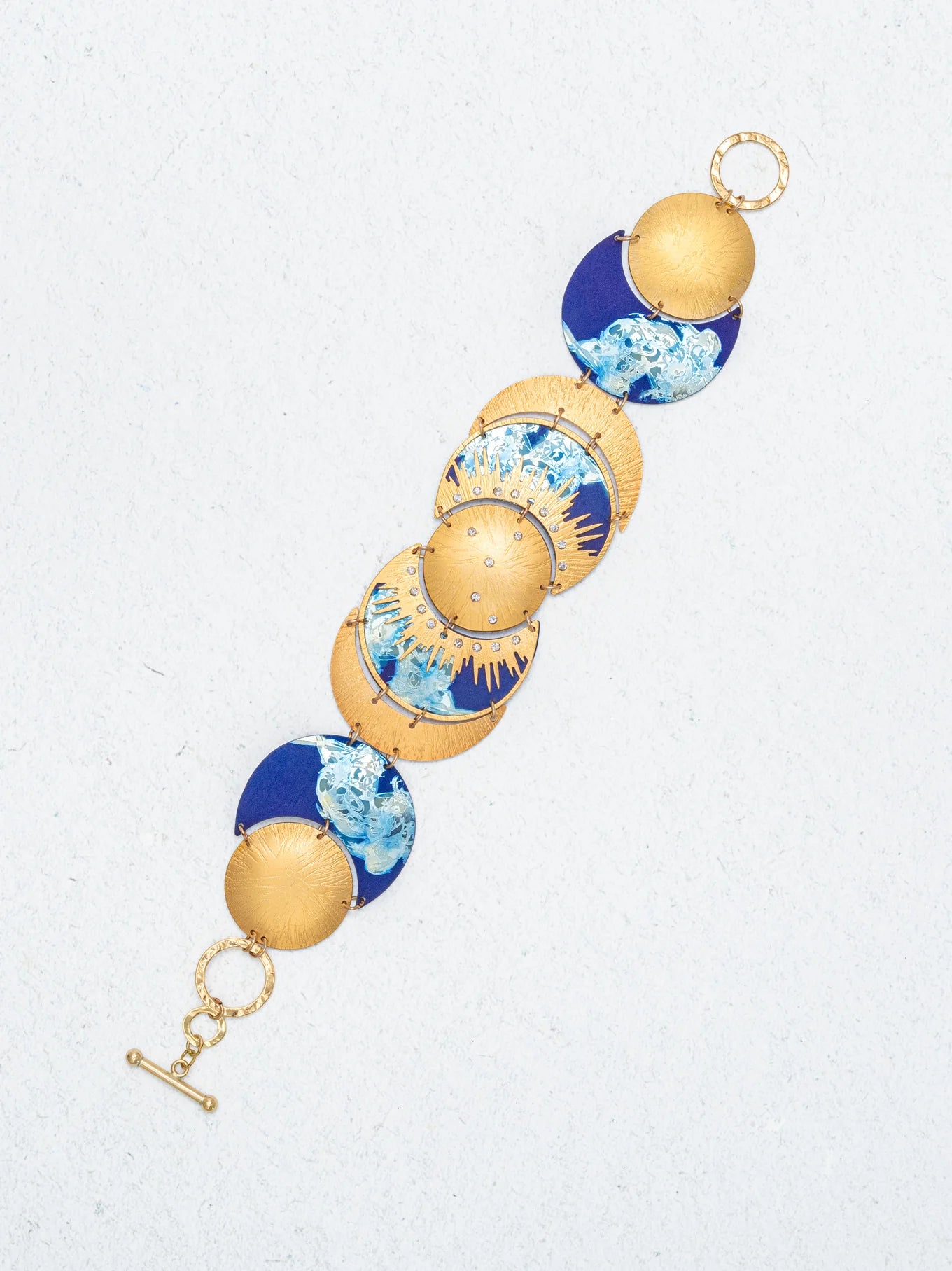 The Selena Midnight Blue Bracelet by Holly Yashi showcases round, domed segments with blue and white marbled designs and a toggle clasp, all displayed on a light textured background for celestial charm.