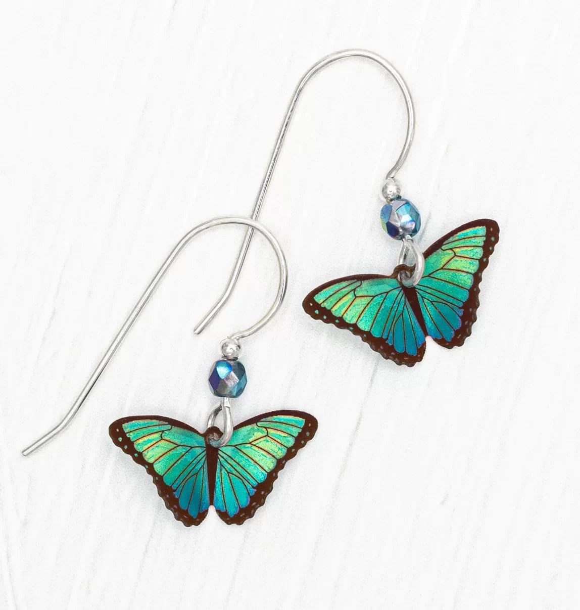 The Green Flash Petite Bella Butterfly Earrings from Holly Yashi feature vibrant blue and green butterfly wings with brown edges. They elegantly hang from sterling silver hooks adorned with small blue beads, showcased beautifully against a crisp white background.