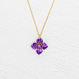 The Petite Fleur Royal Purple Necklace by Holly Yashi features a gold chain and a purple flower-shaped Austrian crystal pendant, shown on a white textured background.