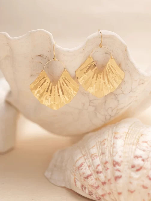 The Gold Ariel Earrings from Holly Yashi are elegantly showcased on white seashells against a neutral background, with their textured and reflective gold plating enhancing the overall elegance.