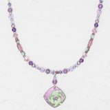 The Elena Beaded Necklace Violet by Holly Yashi features purple, pink, and green beads with a square floral green and purple pendant, shown on a textured white background.