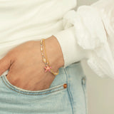 A person in light blue denim jeans, with a hand tucked in their pocket, showcases their wrist adorned with the Carmel Beaded Seashore Blue Starfish Bracelet from Holly Yashi Jewelry. The gold charm features a pink star, beautifully contrasting their white textured long-sleeve top.