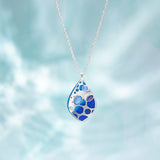 The Seashore Dreams Blue Depths Necklace by Holly Yashi is a silver masterpiece with an aqua-blue teardrop pendant adorned in various blue Austrian crystals, evoking serene ocean waves.