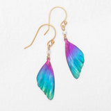The Holly Yashi Blue Violet Flutterby Monarch Earrings feature a stunning gradient of blue, purple, and pink on wing-shaped designs attached to 18k gold-filled French wires, embodying elegance and vibrant charm.