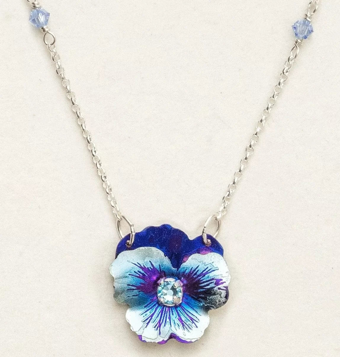 Presenting the Bonnie Blue Garden Pansy Necklace by Holly Yashi, an exquisite niobium piece with a hypo-allergenic silver chain and a stunning blue-purple flower centerpiece featuring a small crystal core.