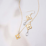 Octavia Gold Silver Earrings by Holly Yashi, inspired by Victorian style, feature clear teardrop crystals and are shown with a gold flower pendant necklace on a soft, light background.