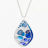 The Seashore Dreams Blue Depths Necklace by Holly Yashi features a silver teardrop pendant with blue, purple, and opalescent stones, accented by Austrian crystals. It hangs elegantly from a delicate chain against a plain white background.