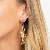 Close-up of a woman with light skin and straight blonde hair wearing Holly Yashi's ER: Gilded Leaf Post Gold earrings—sculptural leaf silhouettes in gold, accented with a small crystal post.