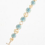 Introducing the Sage Oceana Bracelet by Holly Yashi: a stunning piece featuring alternating blue niobium links with intricate sand dollar motifs and 18k gold-plated links with elegant open circle designs, all showcased on a white speckled background.