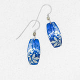 Falling Bloom Indigo Earrings by Holly Yashi: blue, oval-shaped handcrafted earrings with silver floral patterns and hooks, displayed on a light textured background.
