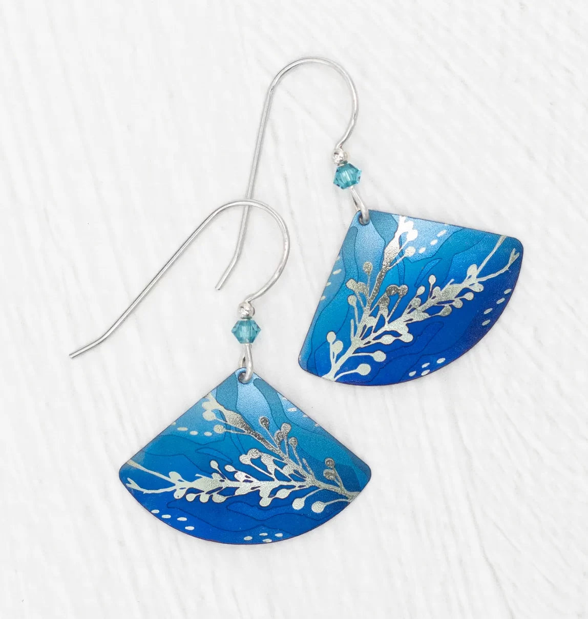 Elegantly experience aquatic beauty with Holly Yashis Sea Meadow Blue and Silver Earrings. These niobium fans feature a leaf pattern, light-to-dark blue gradient, white dots, and delicate blue beads on silver hooks.