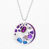 The Ocean Depths Sea Plum Necklace by Holly Yashi features a silver pendant with an abstract design, showcasing purple, blue, and pink Austrian crystals. These varied stones are set within the round pendant on a textured silver chain, offering a colorful and artistic look.