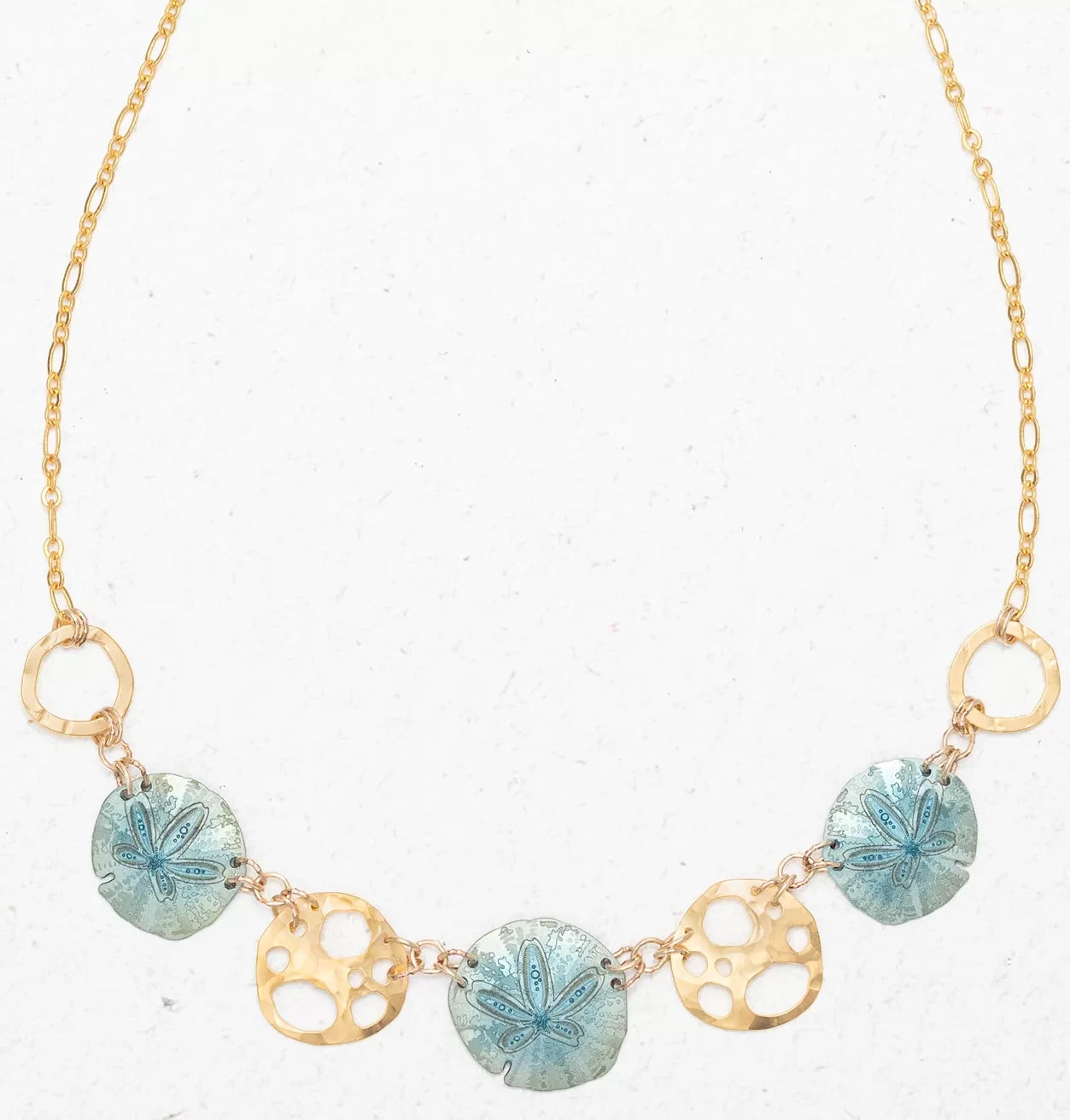 Introducing the Sage Oceana Necklace by Holly Yashi: a gold treasure with alternating blue starfish-patterned pendants and openwork circles like gold-plated shells. The delicate chains small links create an elegant, ocean-inspired ensemble.