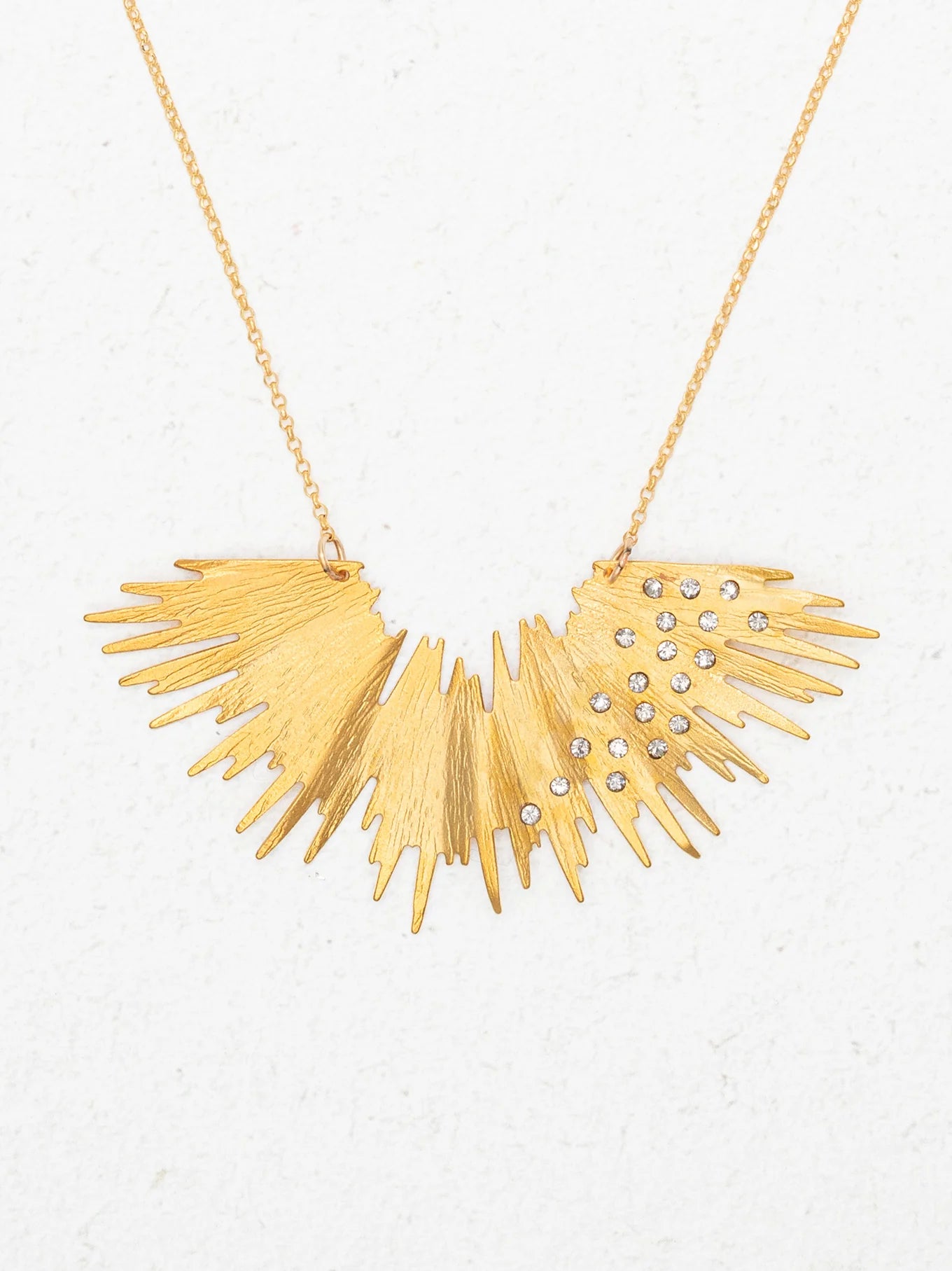 The Aster Necklace-Gold Necklace by Holly Yashi features a sunburst design with jagged rays and sparkling crystals, radiating golden brilliance against a plain white background.