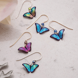 Discover the Holly Yashi Blue Petite Bella Butterfly Earrings, a handcrafted collection with five colorful pairs in shades like blue and purple. Each delicate butterfly sits gracefully on golden hooks, elegantly displayed on a light speckled surface for an exquisite presentation.