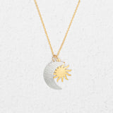 The Holly Yashi Sun and Moon Gold & Silver Necklace features overlapping silver crescent moon and gold sun pendants, reflecting a celestial jewelry style, displayed on a white textured background.