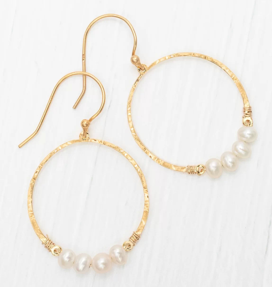 The Rosa Gold and Pearls Hoop Earrings by Holly Yashi feature a hammered texture with five freeform pearls at the bottom, hook fastenings, and are elegantly displayed on a white surface.