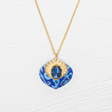 The Arabella Sapphire Blue Necklace by Holly Yashi features a vibrant glass stone set in textured gold with an adjustable pendant for the perfect fit.