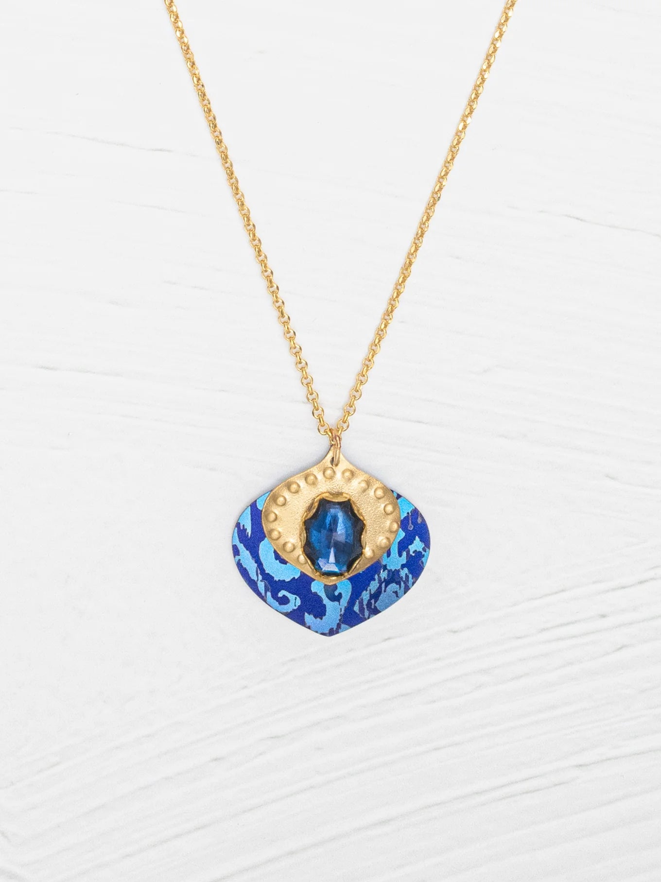 The Arabella Sapphire Blue Necklace by Holly Yashi features a vibrant glass stone set in textured gold with an adjustable pendant for the perfect fit.