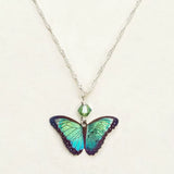 The Green Flash Bella Butterfly Necklace by Holly Yashi features a striking blue and green butterfly pendant on a sterling silver chain, enhanced with a small green crystal bead. Its vibrant wings create an eye-catching centerpiece against the plain background.