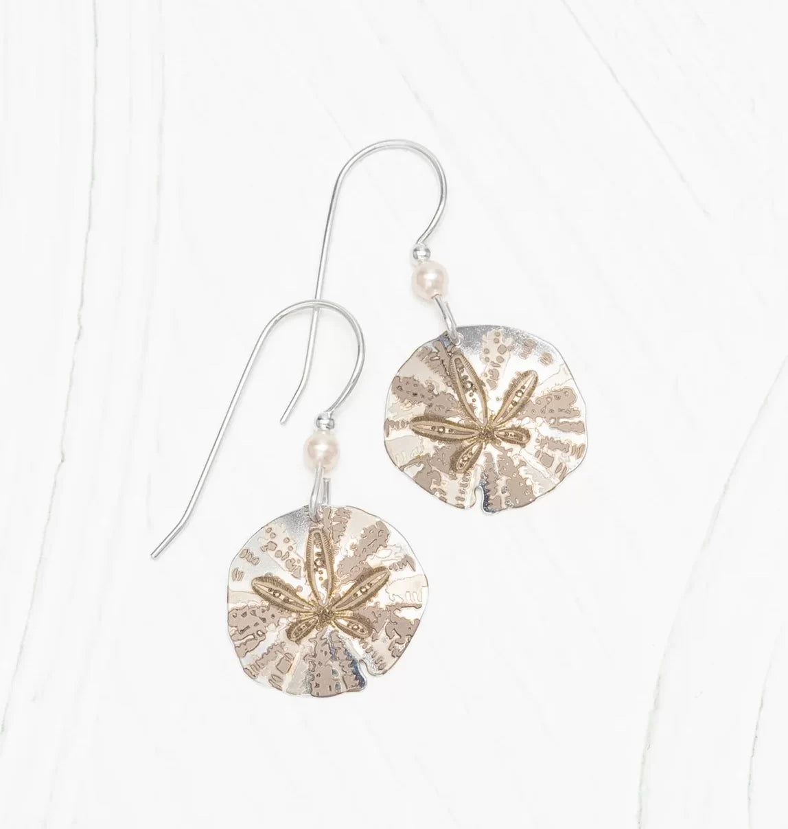 Explore the Holly Yashi Silver Sandra Shore Sand Dollar Earrings, hypo-allergenic sterling silver dangles with gold-tone starfish designs and small pearls near the hooks, all set on a white textured background.