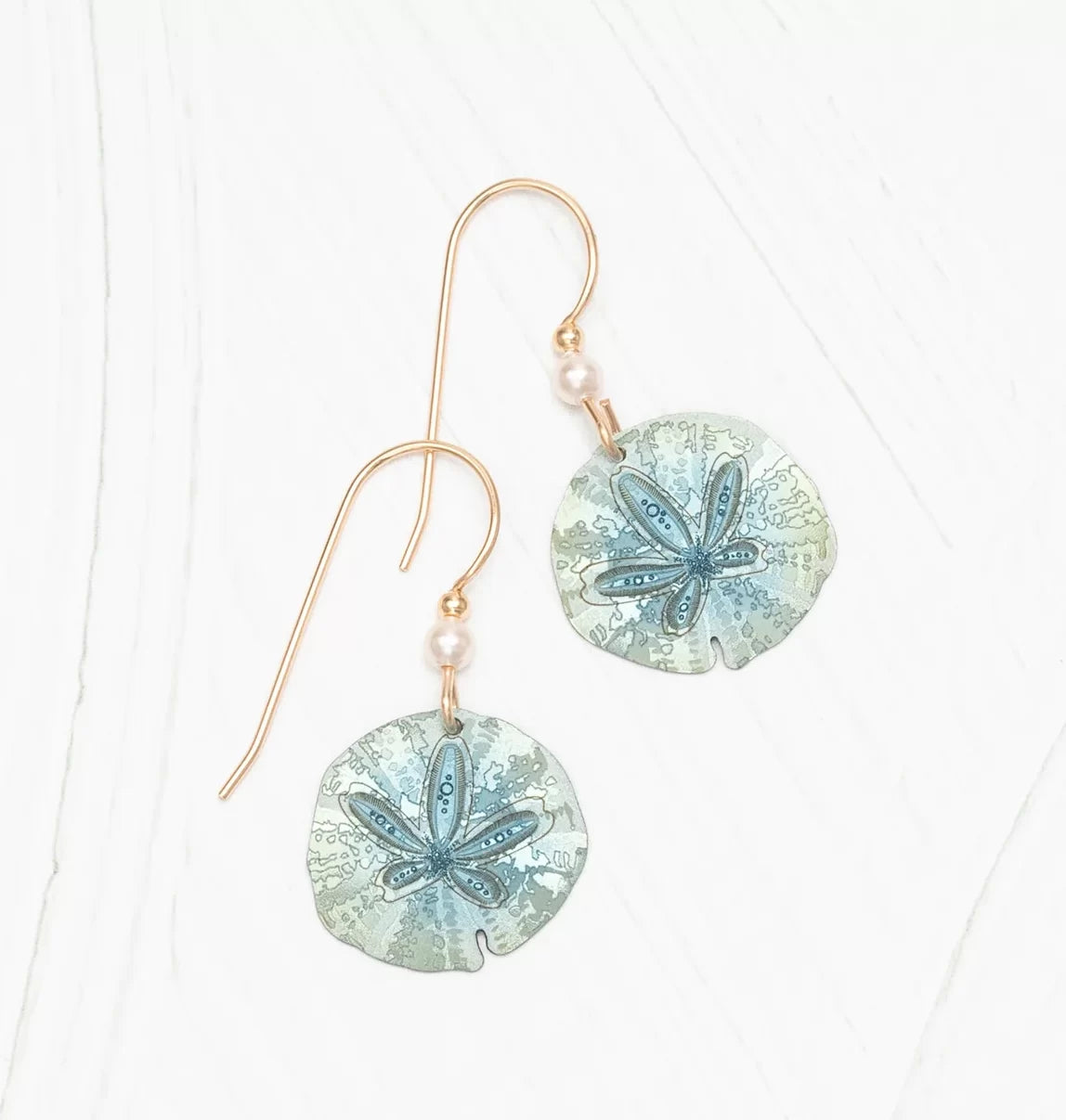 The Sage Sandra Shore Sand Dollar Earrings by Holly Yashi feature exquisite 18k gold-filled wire hooks with translucent circular pendants, accented with delicate blue details and small pearls.
