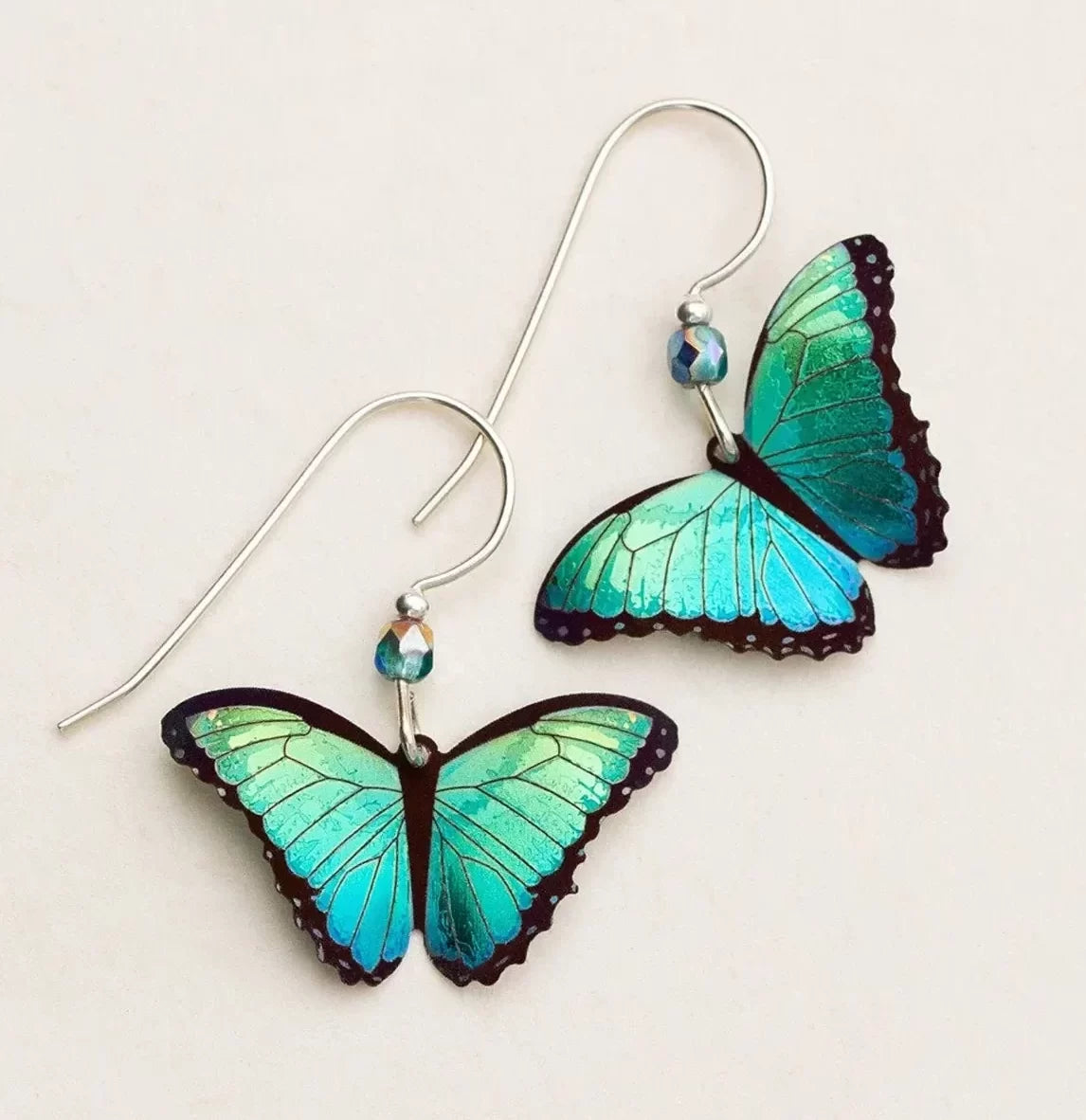 Introducing Holly Yashis Green Flash Bella Butterfly Earrings, featuring turquoise-winged butterflies with dark outlines, silver hooks, and a small blue bead for niobium elegance.