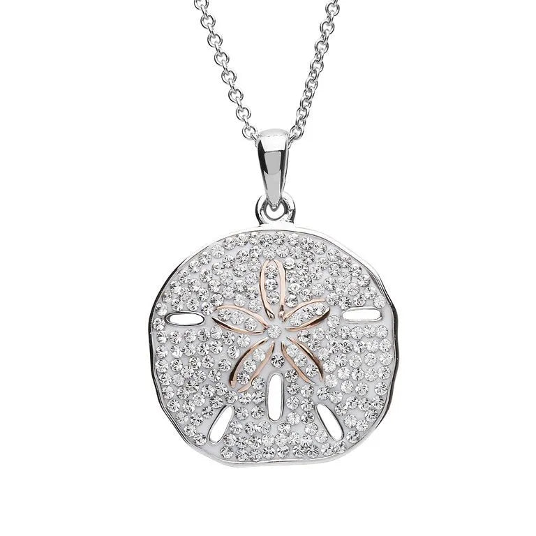 The Shanore Swarovski Crystals White Sand Dollar Necklace features a pendant resembling its namesake, adorned with tiny Swarovski crystals. The central star pattern glistens beautifully on a sterling silver chain, exemplifying elegant ocean jewelry.