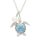 The Shanore Swarovski Crystals Aqua Turtle and Pearl Necklace features a silver pendant with an outstretched-limb turtle and a blue, crystal-encrusted shell, accompanied by a round white pearl charm on a delicate chain for elegance.