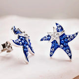 Shanores Swarovski Crystals Blue Sapphire Starfish and Baby Stud Earrings, featuring blue and clear crystals, glisten on a soft white surface. Their intricate design shines under the light, embodying an oceanic theme with Blue Sapphire charm.