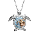 The Shanore Swarovski Crystals Aqua Turtle and Baby Necklace-Ocean Jewelry features a sterling silver turtle pendant with Swarovski crystals, showcasing a gold baby turtle at its center. This stunning piece hangs gracefully from a delicate chain and is set against a pristine white background.