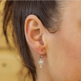 A close-up shows a persons ear adorned with Shanores Swarovski Crystals White Palm Tree Drop Earrings-Ocean Jewelry, highlighting the intricate design and shimmer of Swarovski crystals against a softly blurred background.