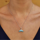 A person wears a Swarovski Crystals Aqua Mermaid Tail Necklace by Shanore, featuring a turquoise mermaid tail pendant on a sterling silver chain, set against a neutral backdrop. They wear a dark V-neck top.