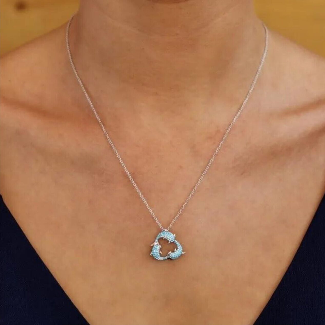 The individual showcases Shanores Swarovski Crystals Three Dolphins Necklace- Ocean Jewelry, worn with a deep V-neck top against a simple, warm-colored background.