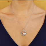 Close-up of a Shanore Swarovski Crystals Circle Mermaid with Pearl Necklace-Ocean Jewelry, featuring a mermaid pendant encircled delicately. The thin chain sparkles with Swarovski Crystals against a warm-toned backdrop, worn over a dark V-neck top.