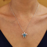 A woman wears a Shanore Swarovski Crystals Teal Filigree Turtle Necklace-Ocean Jewelry, which gracefully sits above her dark V-neck top.